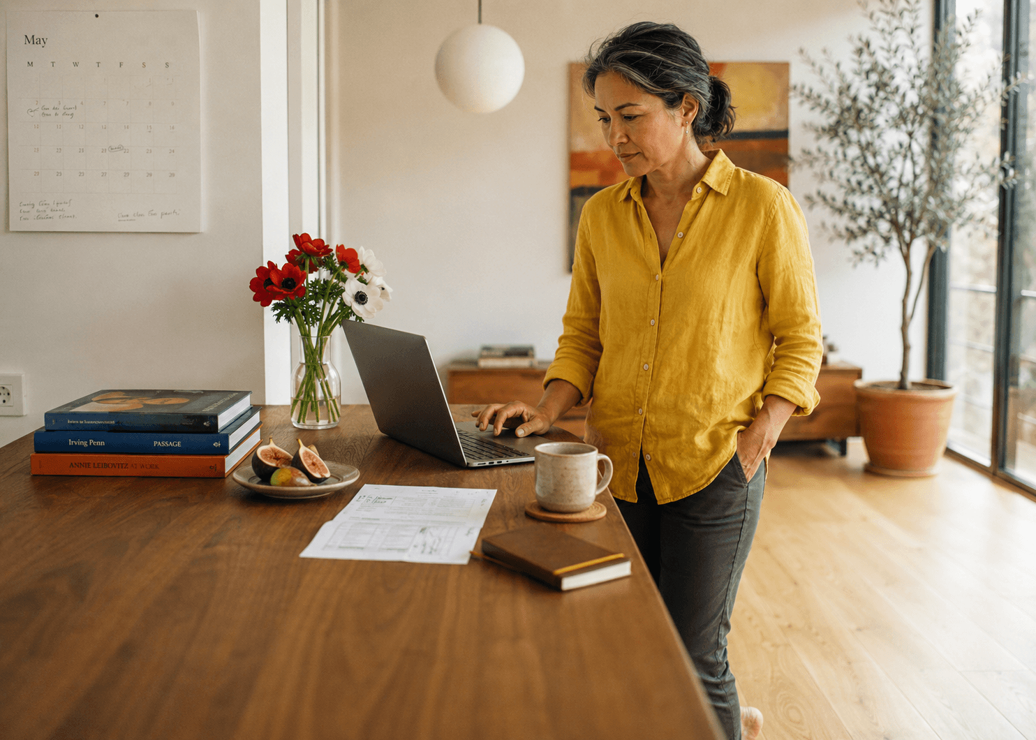 A woman checks her laptop at a kitchen table in the morning light